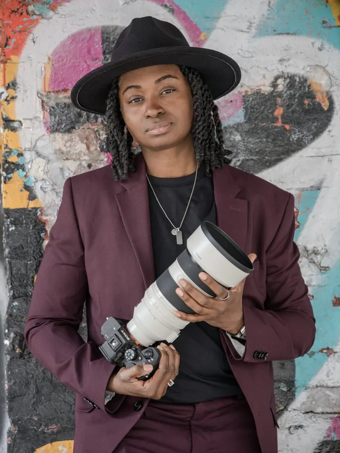 Kash holding her camera and telephoto lens in front of a graffiti wall
