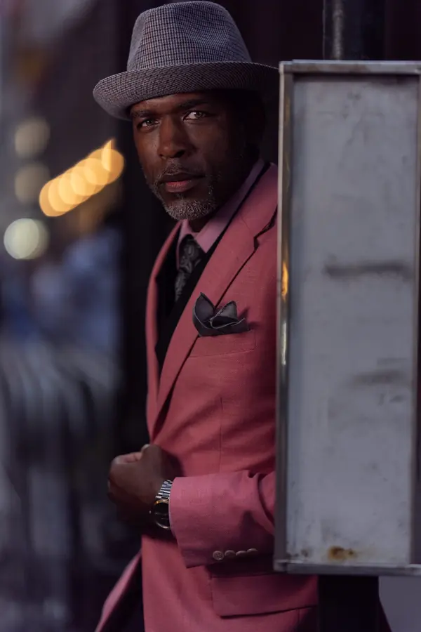 Man in a pink suit and fedora in a city doorway at night