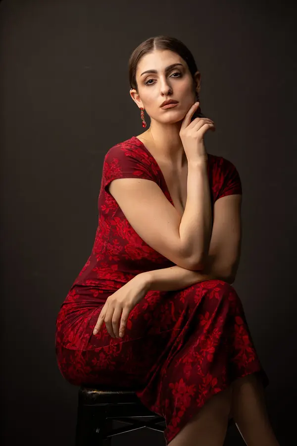 Woman in a red dress seated against a dark backdrop