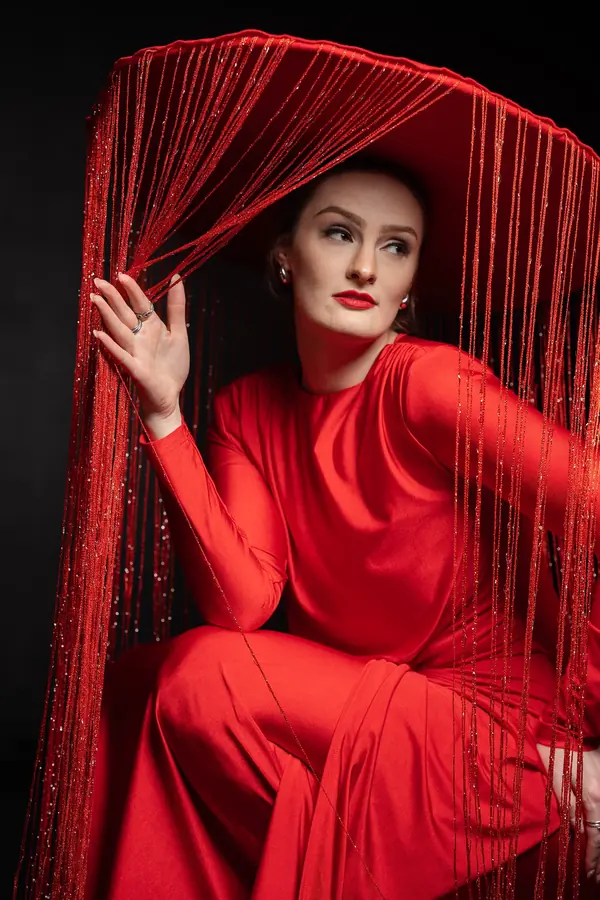 Woman in red seated beneath a curtain of red fringe